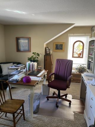 Original photograph of the existing office layout with a desk of paperwork, purple office chair, sloped wall and shelving