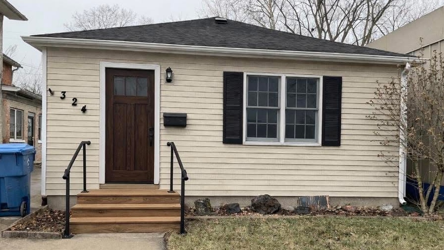 Original downtown rental residence with light siding, dark front door and a simple lawn