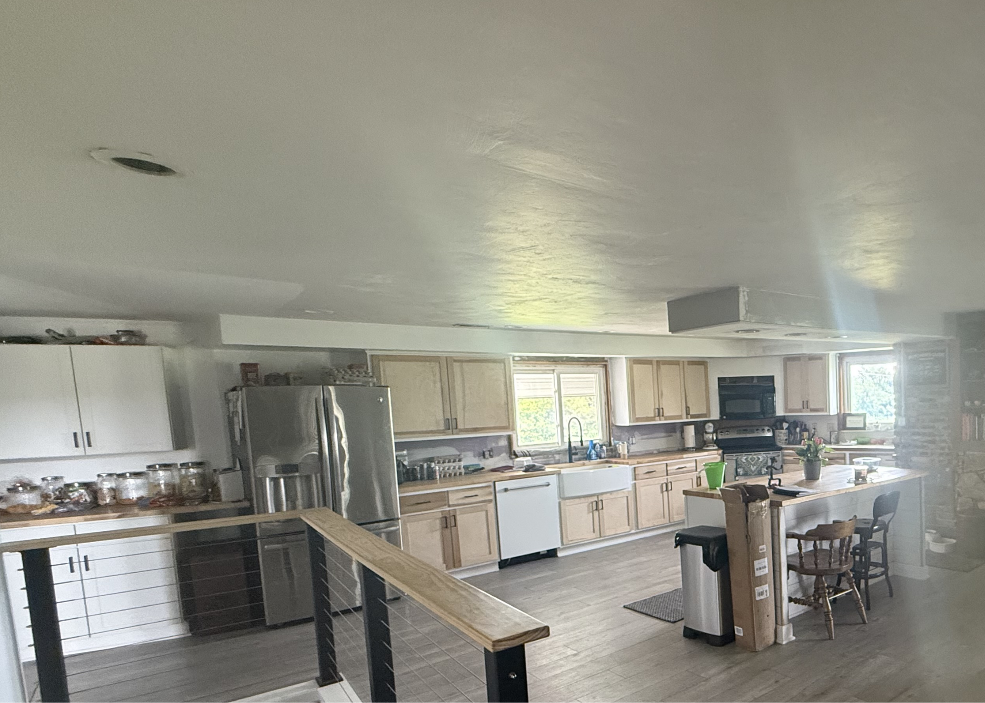 Original photograph of the existing kitchen with cabinets, refrigerator, island and stair railing