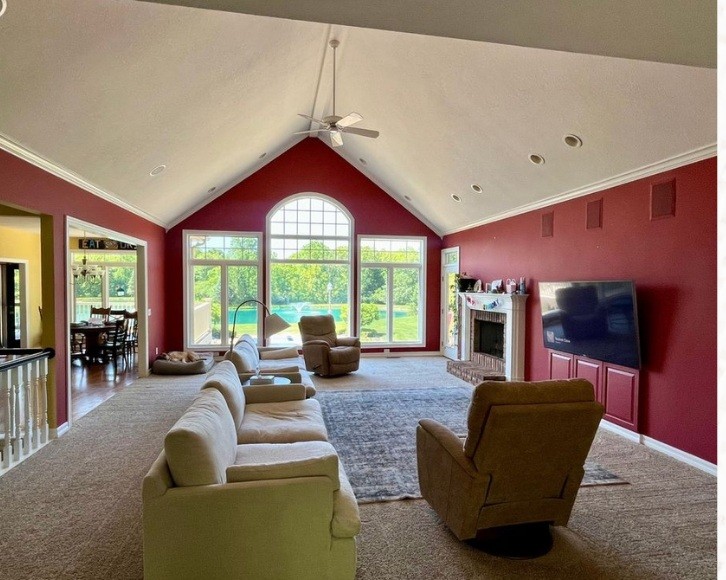 Original living room with deep red walls, carpet, a vaulted ceiling and tall arched windows